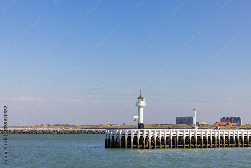 A picturesque lighthouse proudly stands tall on a wooden pier, overlooking serene and calm waters on a bright sunny day A picturesque lighthouse proudly stands tall on a wooden pier, overlooking serene and calm waters on a bright sunny day
