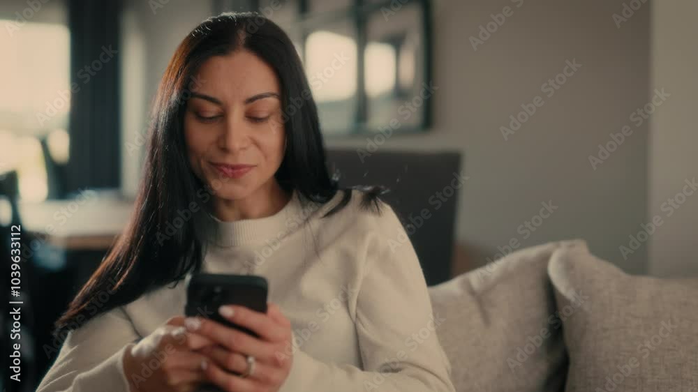  Woman holding smartphone sitting on couch at home Woman with cell phone surfing internet using social media apps. Shopping online Internet news cellphone. Talking on the phone