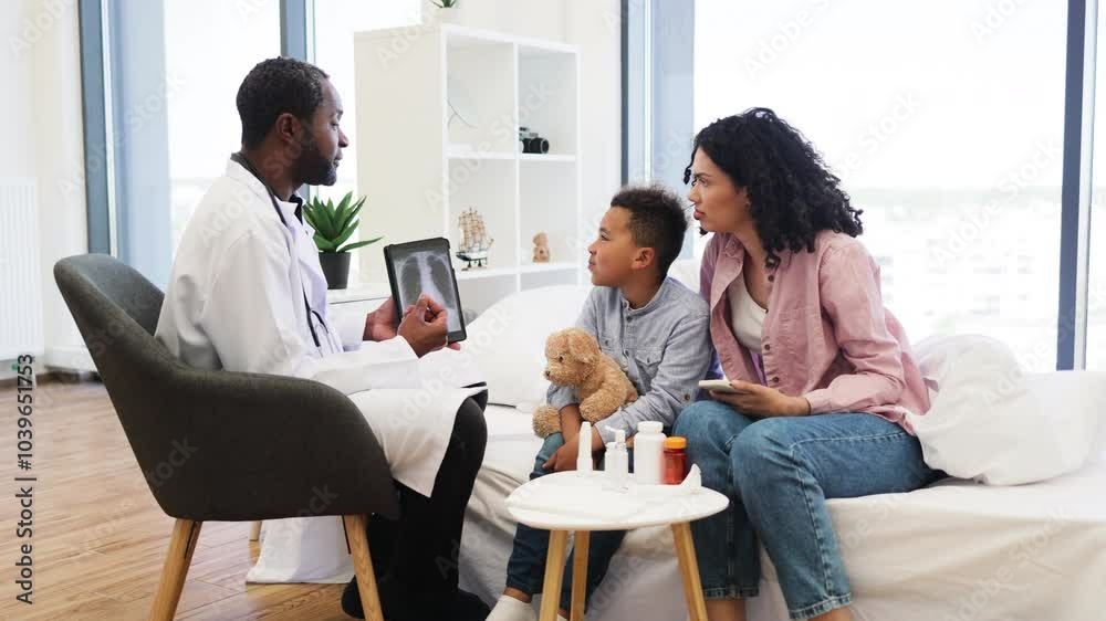 African doctor discussing x-ray results with concerned mother and young son in modern clinic. Male child showing interest in digital tablet while mother listens attentively. African doctor discussing x-ray results with concerned mother and young son in modern clinic. Male child showing interest in digital tablet while mother listens attentively.