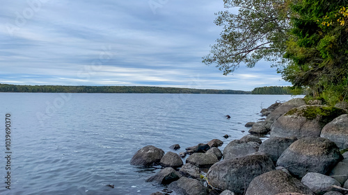 Serene lakeside view with rocky shoreline under cloudy sky, ideal for nature retreats and tranquility during midsummer celebrations