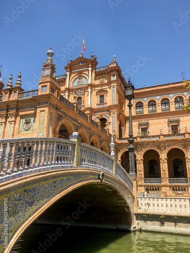 Ornate bridge and historic architecture of Plaza de Espana in Seville under clear blue sky, capturing Spanish cultural heritage