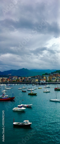 Tranquil harbor scene with boats anchored under cloudy skies, ideal for illustrating travel or coastal living concepts