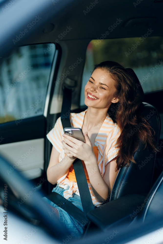 Naklejka premium young woman sitting in a car, smiling while using a smartphone, modern interior, casual outfit, comfortable atmosphere, enjoying leisure time, connected lifestyle, sunny day