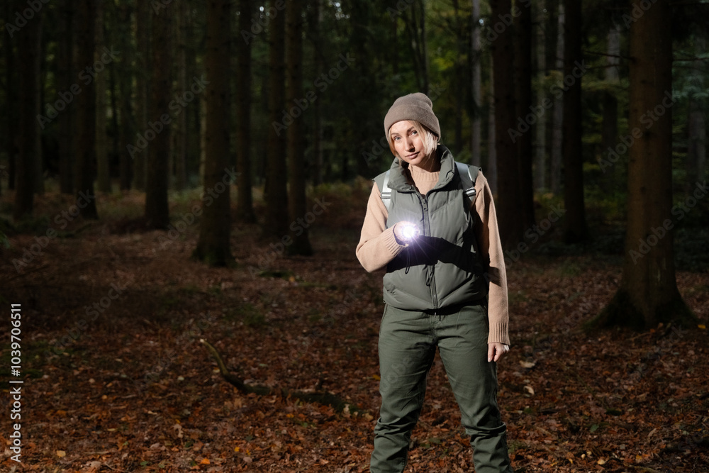 a female tourist with a backpack walks through a dark forest and finds something in it. She shines a lantern on the spot and points at it. concept of fear, halloween, animal watching. free space a female tourist with a backpack walks through a dark forest and finds something in it. She shines a lantern on the spot and points at it. concept of fear, halloween, animal watching. free space