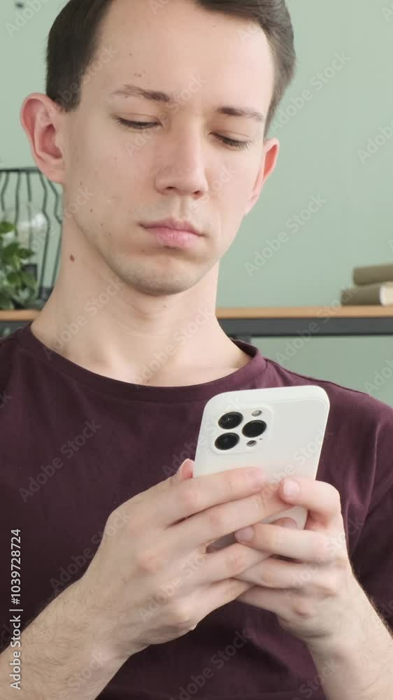Thoughtful young adult Caucasian man chatting in online social media using cellphone at home. Concept of a remote communication. Vertical video. Thoughtful young adult Caucasian man chatting in online social media using cellphone at home. Concept of a remote communication. Vertical video.