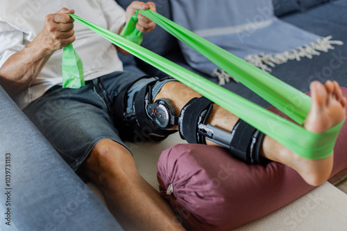 Part of Senior Man performing rehabilitation exercises using resistance equipment to aid in his knee recovery process. A Physical Therapy Exercise with leg brace. Unrecognizable, cropped. Horizontal. 