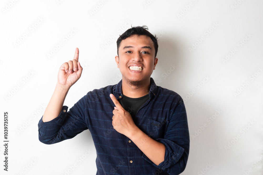 Fototapeta premium Adult Asian man looking at camera with happy expression while pointing up with two finger