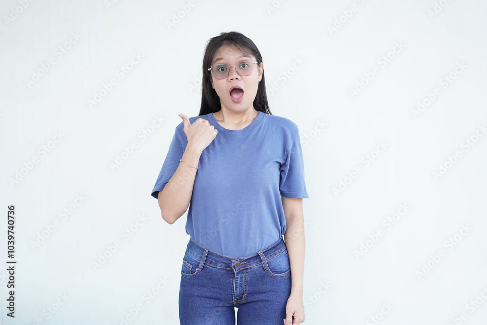Beautiful Asian woman points to the side with her thumb, suggesting a promotion or advertisement on a white background Beautiful Asian woman points to the side with her thumb, suggesting a promotion or advertisement on a white background