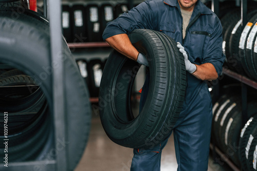 In gloves, professional worker with tire. Man is in the tire fitting car service