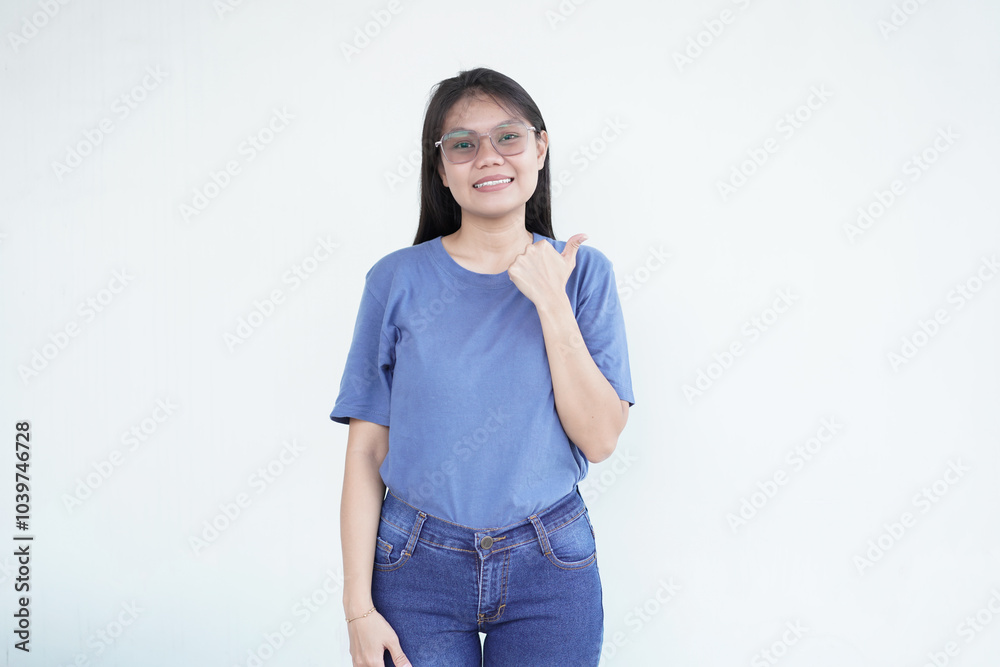 Beautiful Asian woman points to the side with her thumb, suggesting a promotion or advertisement on a white background Beautiful Asian woman points to the side with her thumb, suggesting a promotion or advertisement on a white background
