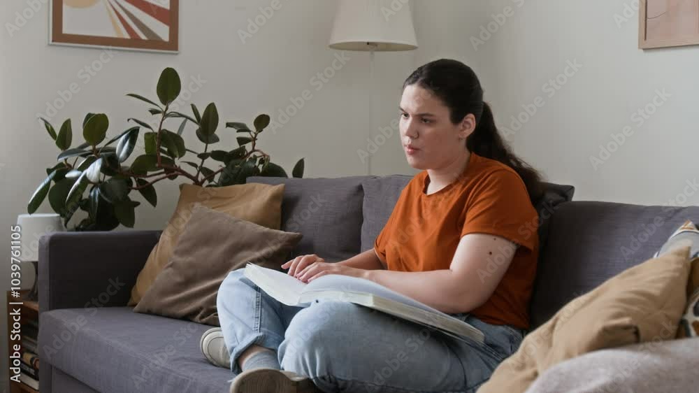 Girl with disability reading book written with braille dot system while relaxing on couch in living room Girl with disability reading book written with braille dot system while relaxing on couch in living room