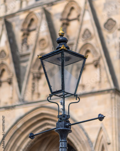 An ornate of wrought iron lamp sits in front of the facade of the south facing tower of York Minster. Carvings in the elaborate gothic architecture are in the background. photo