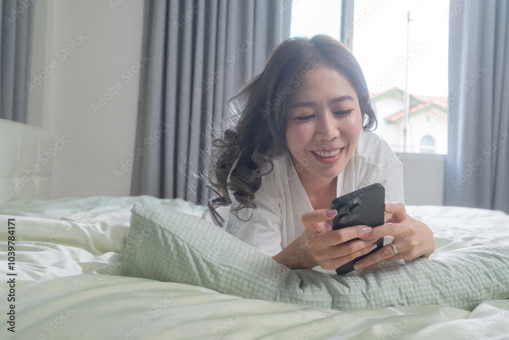 A woman lying comfortably on a bed, smiling while focused on her smartphone and tablet. The bright and cozy atmosphere captures a cheerful moment of happiness in her personal space. A woman lying comfortably on a bed, smiling while focused on her smartphone and tablet. The bright and cozy atmosphere captures a cheerful moment of happiness in her personal space.
