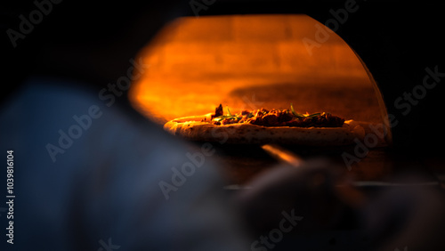 Traditional Italian pizzeria, chef places a pizza onto stone in wood fired oven