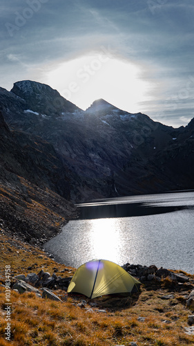 A yellow tent by a mountain lake in the Alps