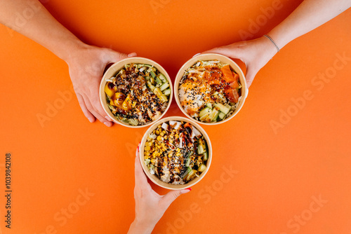 Hands holding vibrant poke bowls on orange background, celebrating healthy eating and shared meals photo