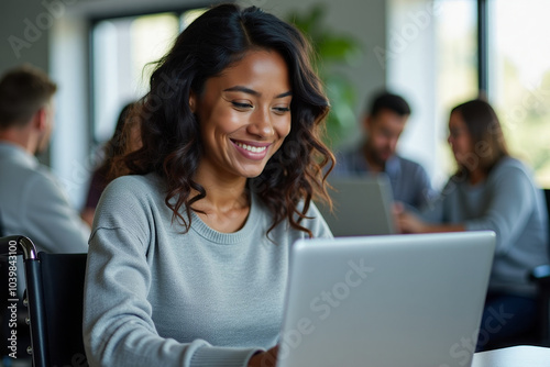 A young African American woman with wavy shoulder-length hair in a light gray sweater sits in a wheelchair and works at a laptop against the background of colleagues Free Download A young African American woman with wavy shoulder-length hair in a light gray sweater sits in a wheelchair and works at a laptop against the background of colleagues - GFXLoad
