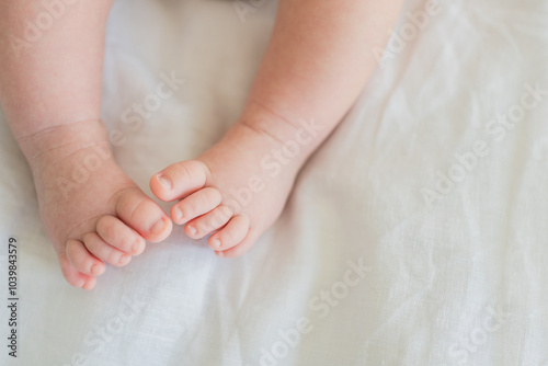 Tiny newborn infant baby feet and toes on white background. Soft newborn baby foot legs under the white blanket. Close up of infant barefeet. Maternity tenderness parenthood birthday. Happy Family