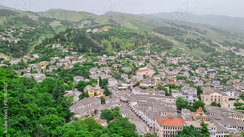 Panoramic view of the city of Gjirokaster, Albania. Nestled in valley between mountains, with a dense cluster of whitewashed houses with traditional layered stone tile roofs. Historical charm. Tourism