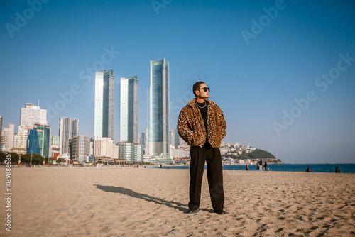 A Korean guy in a leopard fur coat walks along the beach against the backdrop of the autumn landscape of Busan Haeundae.