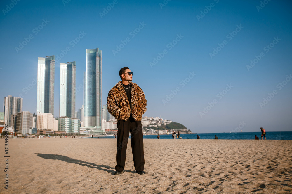 A Korean guy in a leopard fur coat walks along the beach against the backdrop of the autumn landscape of Busan Haeundae.