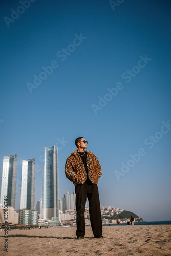 Obraz na płótnie A Korean guy in a leopard fur coat walks along the beach against the backdrop of the autumn landscape of Busan Haeundae. w salonie