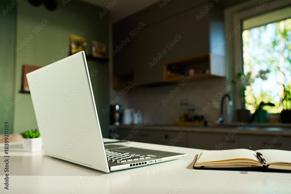 Minimalist home office with laptop, small potted plants and coffee mug on white desk with kitchen interior in background. Workspace for distant work from home Minimalist home office with laptop, small potted plants and coffee mug on white desk with kitchen interior in background. Workspace for distant work from home