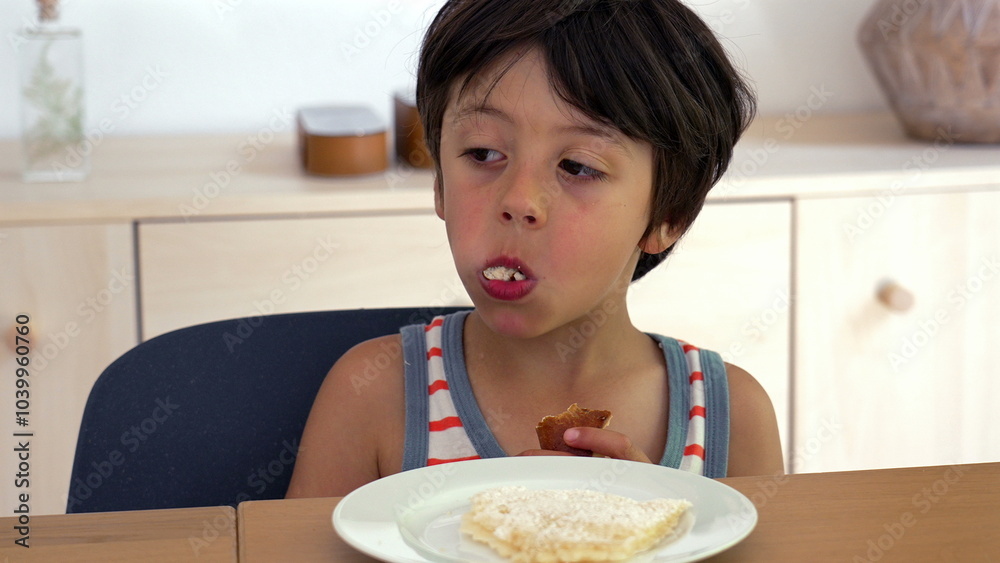 Young boy eating bread at the dining table, chewing and enjoying his food in a casual home setting, with focus on his thoughtful expression during mealtime