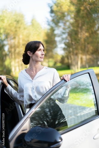 Woman standing by car in sunlit park