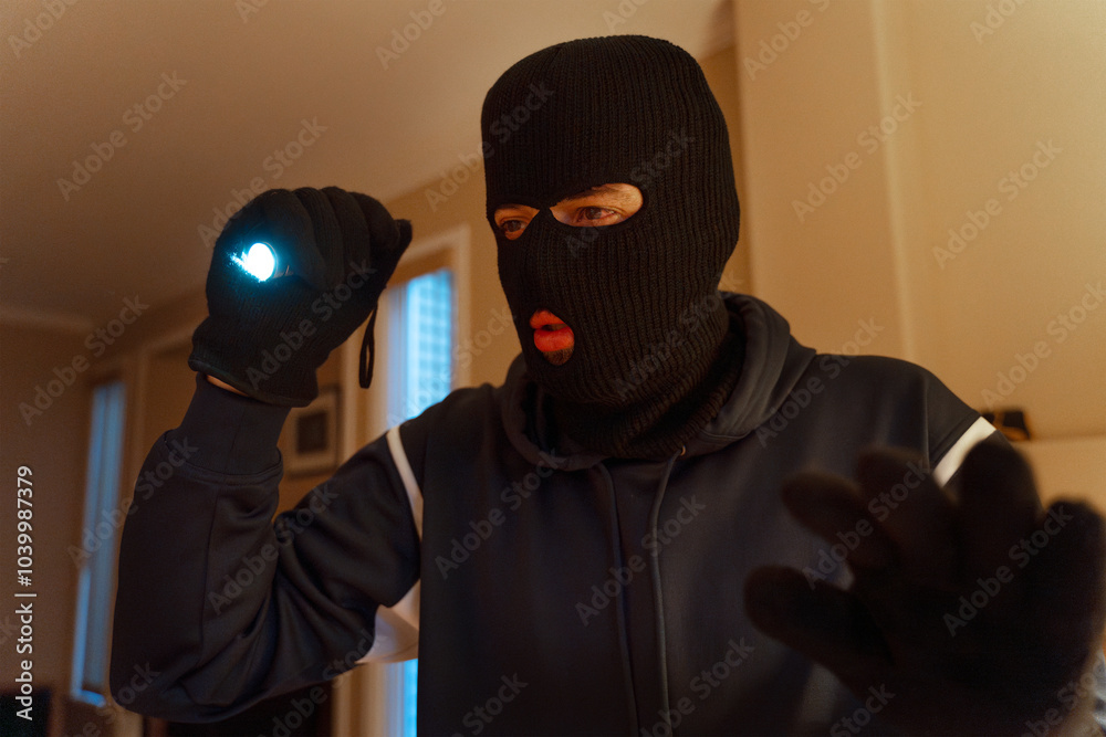Masked burglar searching home at night using flashlight Masked burglar searching home at night using flashlight