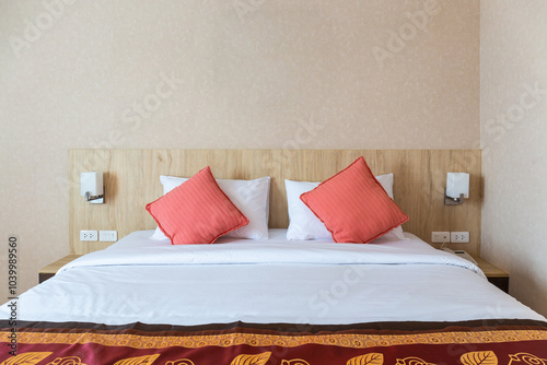 Double red and white pillows on a wooden bed with power outlets and bedside lamps photo