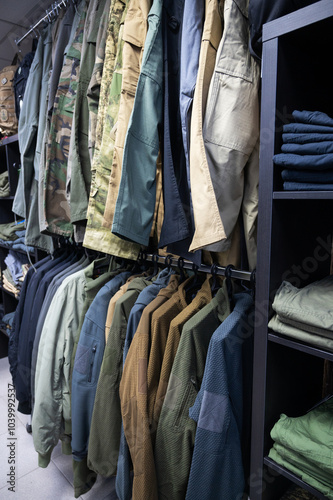 Stacked tactical pants and military uniforms, including camouflage and outdoor gear, neatly arranged on dark wooden shelves in a store.