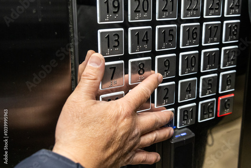 Hand reaching out to elevator panel's braille codes to press button for floor level destination of building