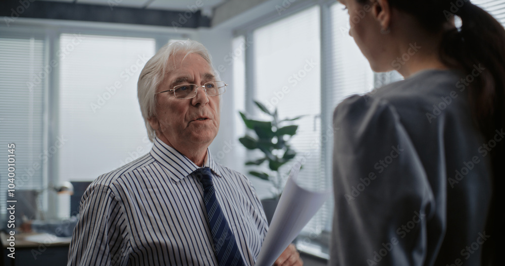 Obraz premium Senior boss of the company with papers talks to female financial specialist. Bank employee discuss business strategy with team leader. Modern office of international corporation. Business concept.