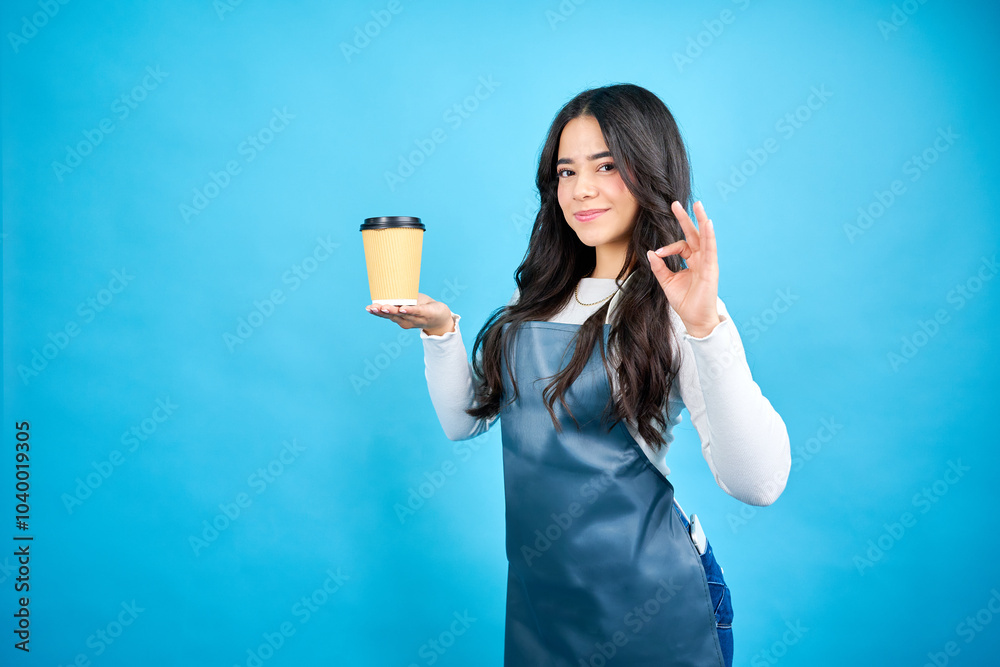 portrait young latin woman holding disposable coffee cup and making ok sing with hand in studio. portrait young latin woman holding disposable coffee cup and making ok sing with hand in studio.