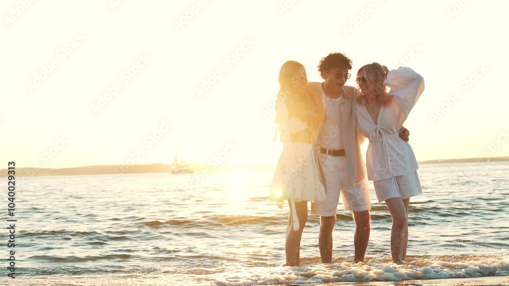 Group of young three smiling friends having fun at the seaside. Man and two cute female at sunset in casual summer clothes. Young women hugging his friend at sunrise. Enjoy their life, relax Group of young three smiling friends having fun at the seaside. Man and two cute female at sunset in casual summer clothes. Young women hugging his friend at sunrise. Enjoy their life, relax