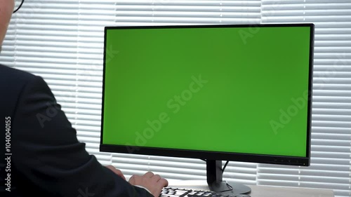Back view of man using computer with green screen at office. Close-up of business man working on computer monitor with chroma key
