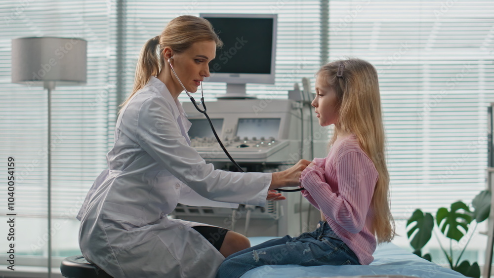 Obraz premium Woman listening kid stethoscope in examination room. Cute child visiting doctor