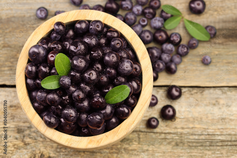 Ripe acai berries and leaves in bowl on wooden table, top view Ripe acai berries and leaves in bowl on wooden table, top view