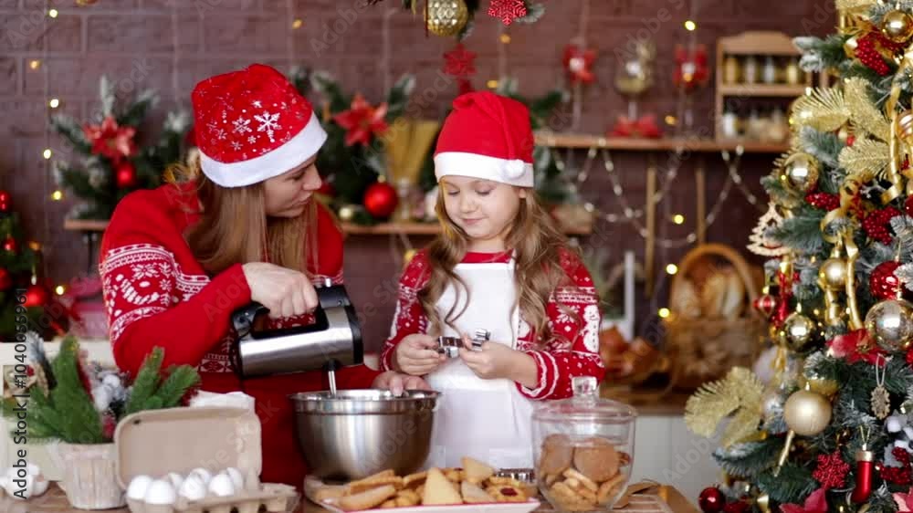 mom and daughter in the kitchen with New Year decor in red Santa Claus hats are preparing a festive dinner playing with flour and having fun and laughing, preparing for the new year.