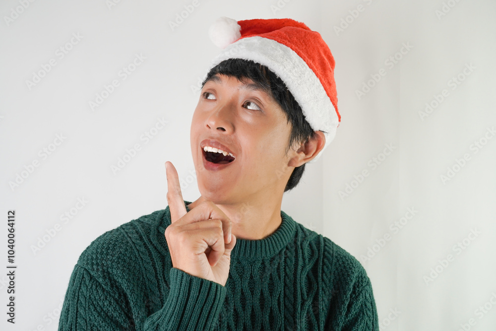 Excited young asian man wearing santa clause hat and green long sleeved sweater with smiling face expression, isolated over white background. Concept for Christmas Holiday and New Year Party Excited young asian man wearing santa clause hat and green long sleeved sweater with smiling face expression, isolated over white background. Concept for Christmas Holiday and New Year Party