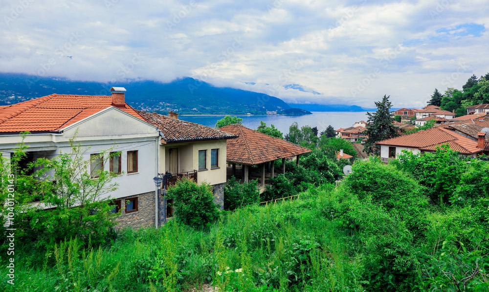 A tranquil view of Ohrid Macedonia showcasing lush greenery and serene lakeside homes under a cloudy sky A tranquil view of Ohrid Macedonia showcasing lush greenery and serene lakeside homes under a cloudy sky
