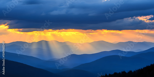 Golden light cascades over distant mountains as the sun sets, creating a dramatic play of shadows and light in the sky