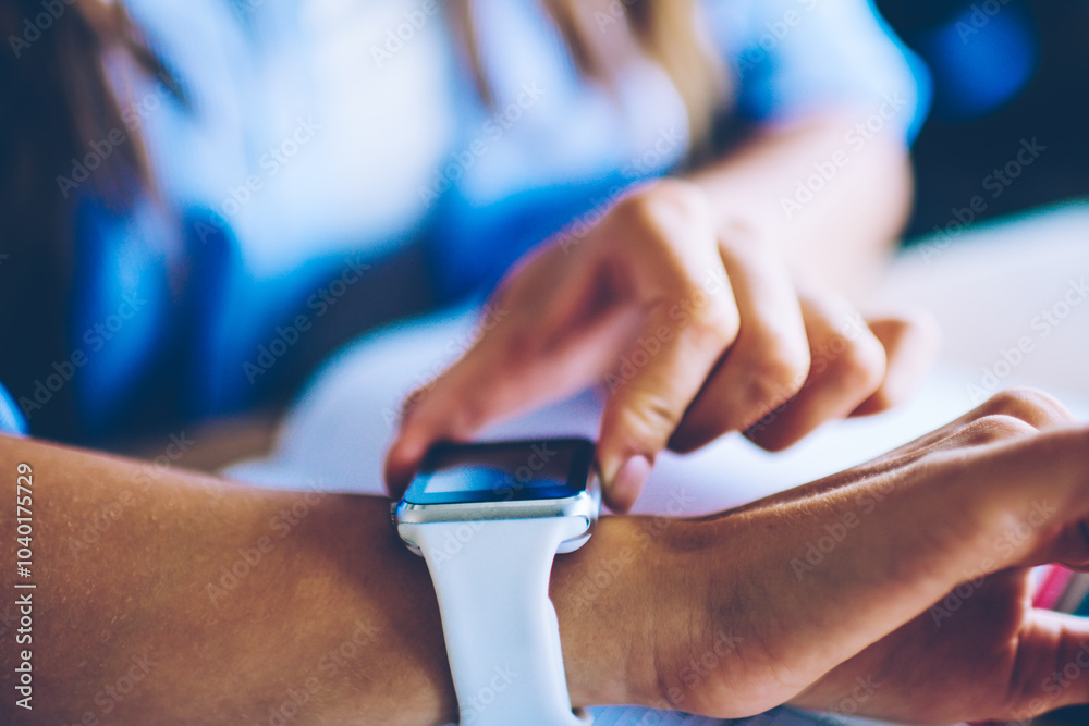 Fototapeta premium Cropped picture of woman sitting at desktop and checking notification on digital wearable wrist watch, selective focus on female hands and new modern smartwatch looking for time to end of work
