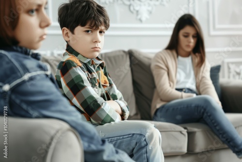 An upset boy sits quietly on the sofa while his mother looks on in concern, reflecting their emotional disconnect during a quiet afternoon