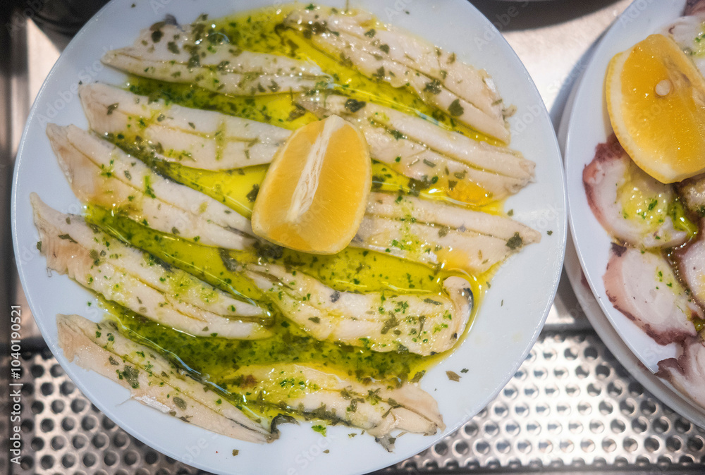 Pickled anchovies with garlic and parsley marinated in vinegar in a round wooden plate on a white wooden table. Typical Spanish snack. Pickled anchovies with garlic and parsley marinated in vinegar in a round wooden plate on a white wooden table. Typical Spanish snack.