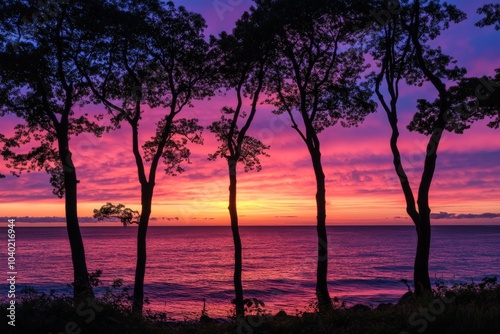 A mesmerizing purple and pink sunset casts its glow over the ocean, with tall trees creating striking silhouettes, offering a peaceful and reflective visual experience.