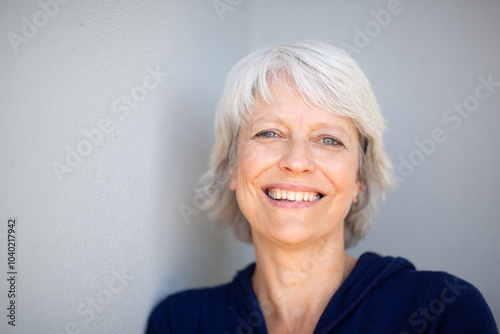 Happy mature woman leaning against gray wall