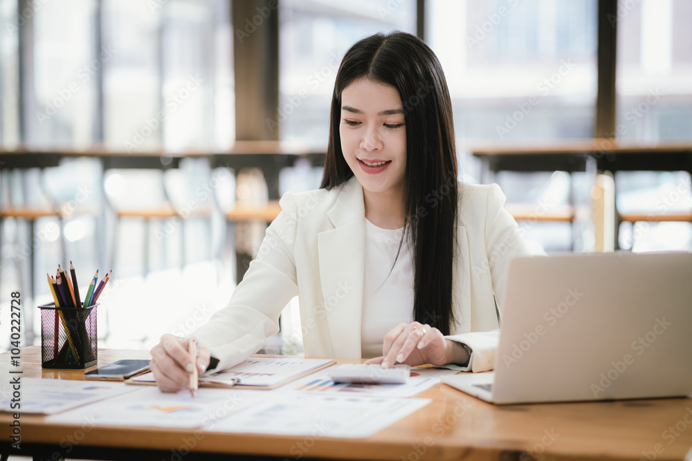 Beautiful Asian female accountant working with smartphone and laptop at her desk analyzing business reports and documents. Sending messages Beautiful Asian female accountant working with smartphone and laptop at her desk analyzing business reports and documents. Sending messages