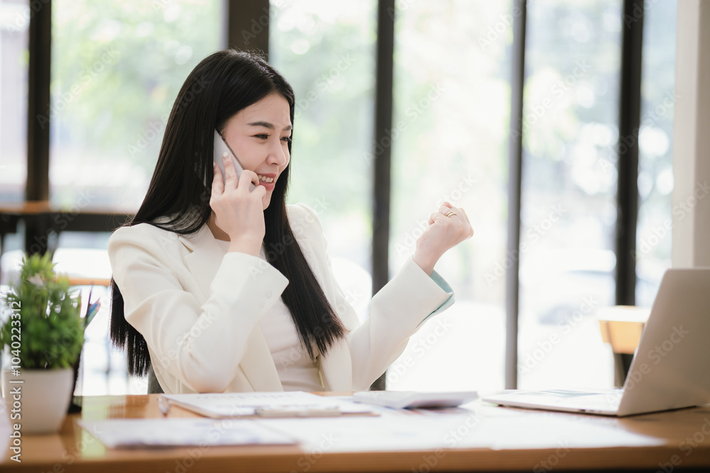 Beautiful Asian female accountant working with smartphone and laptop at her desk analyzing business reports and documents. Sending messages Beautiful Asian female accountant working with smartphone and laptop at her desk analyzing business reports and documents. Sending messages